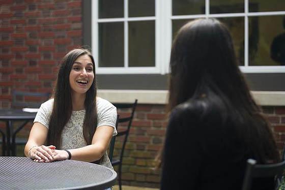 Photo of two young women speaking animatedly at a table outside